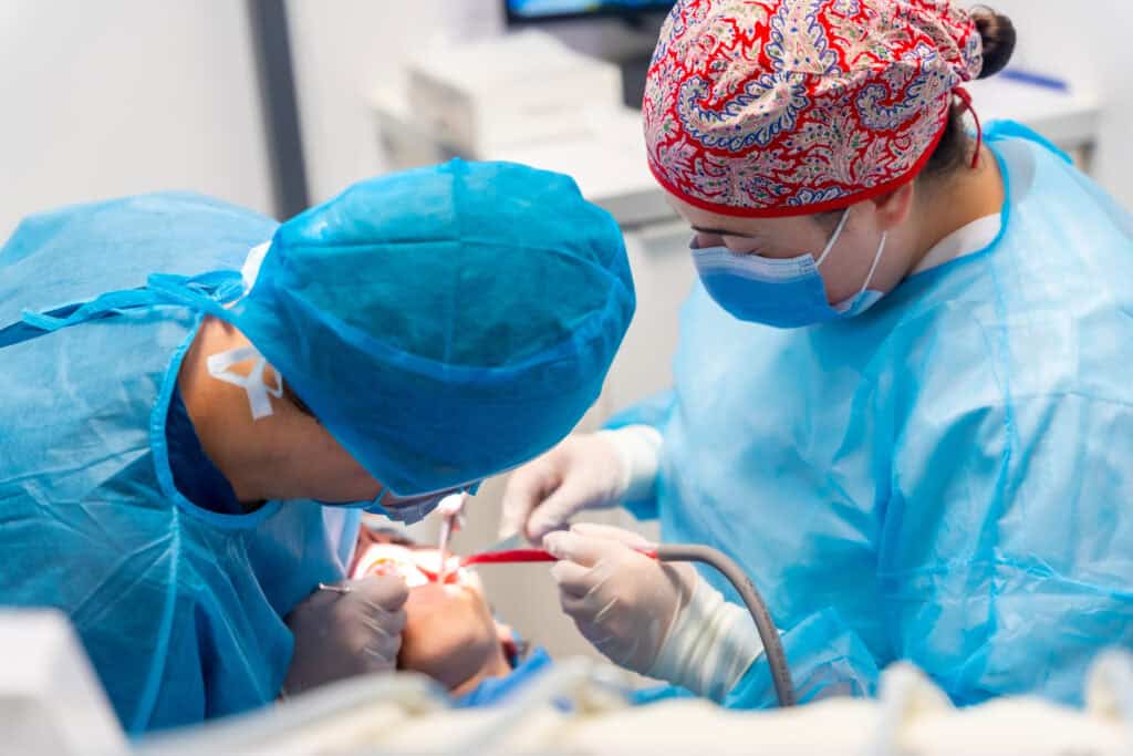 Female surgeons in blue overalls and hats performing oral surgery